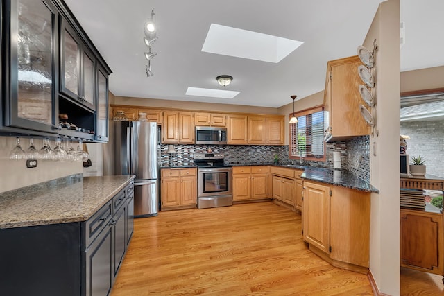 kitchen featuring a sink, stainless steel appliances, light wood-type flooring, backsplash, and a skylight
