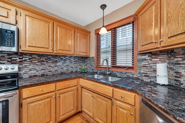 kitchen featuring dark stone counters, a sink, backsplash, hanging light fixtures, and stainless steel appliances