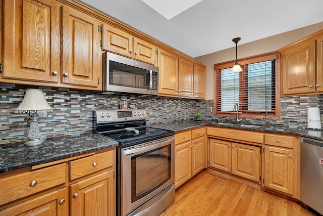 kitchen featuring appliances with stainless steel finishes, tasteful backsplash, light wood-type flooring, a sink, and dark stone counters