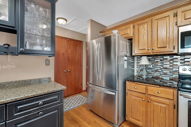 kitchen featuring light wood-style floors, glass insert cabinets, decorative backsplash, and stainless steel appliances