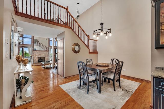 dining area with an inviting chandelier, baseboards, a stone fireplace, a high ceiling, and light wood finished floors