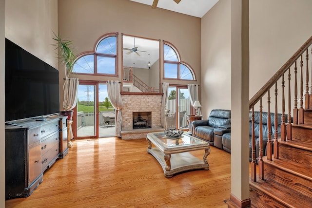 living area with a towering ceiling, ceiling fan, stairs, and light wood finished floors