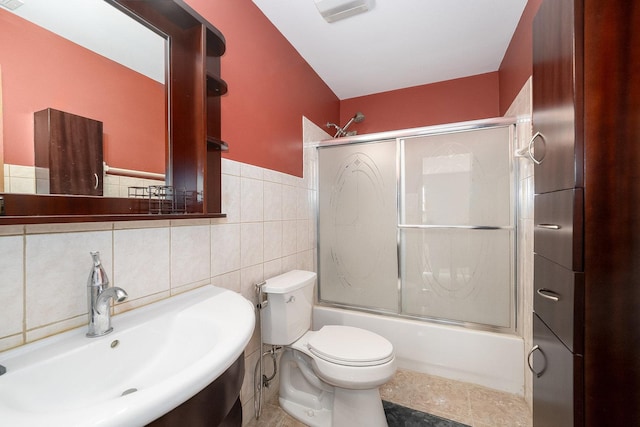 bathroom with visible vents, tile walls, a sink, toilet, and enclosed tub / shower combo