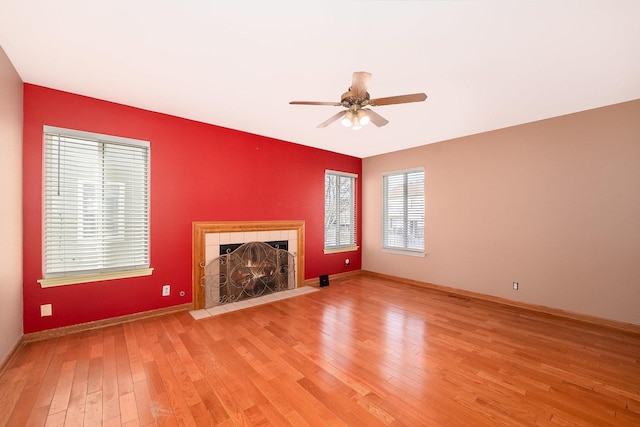 unfurnished living room with a fireplace, ceiling fan, baseboards, and light wood-type flooring