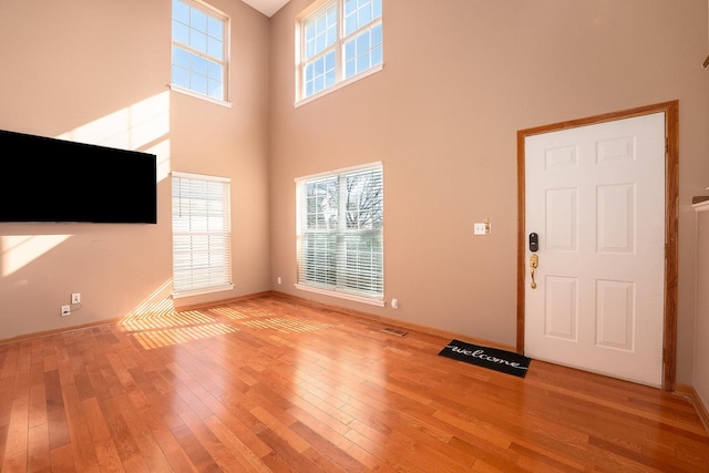 unfurnished living room with plenty of natural light, baseboards, a high ceiling, and light wood-type flooring