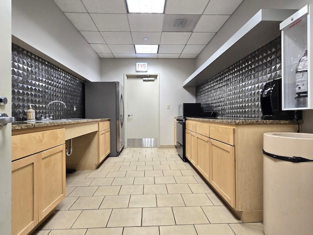 kitchen featuring light brown cabinetry, a drop ceiling, freestanding refrigerator, and black range with electric cooktop