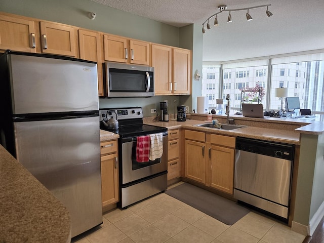 kitchen with a textured ceiling, a sink, a peninsula, light brown cabinets, and stainless steel appliances