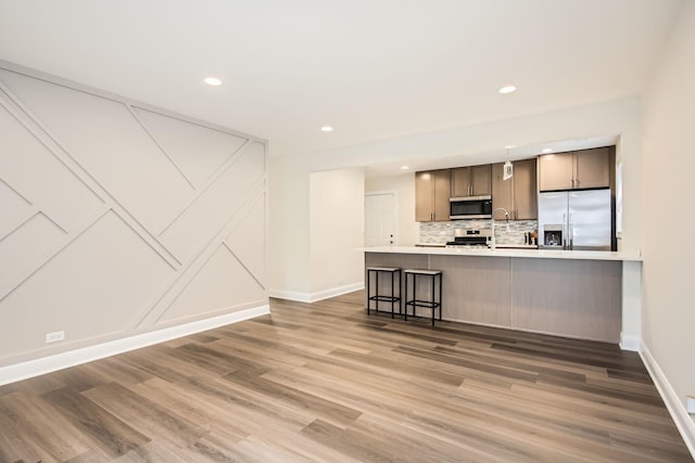 kitchen with appliances with stainless steel finishes, light countertops, baseboards, wood finished floors, and backsplash