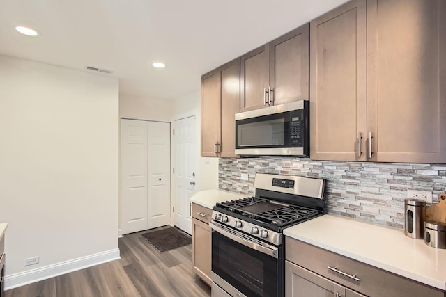 kitchen with appliances with stainless steel finishes, light countertops, dark wood finished floors, backsplash, and visible vents