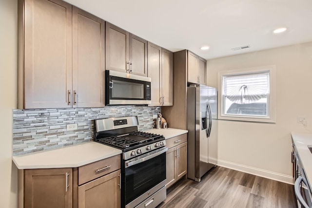 kitchen with dark wood-style flooring, appliances with stainless steel finishes, light countertops, backsplash, and visible vents