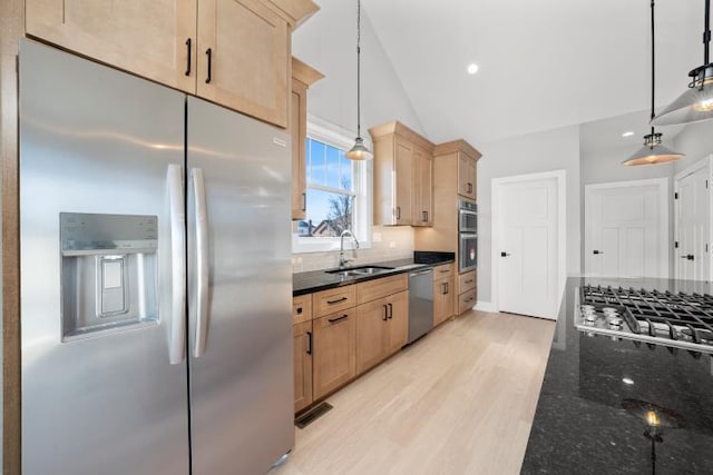 kitchen featuring appliances with stainless steel finishes, a sink, light wood finished floors, and dark stone countertops