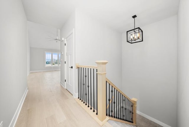 hall featuring baseboards, wood finished floors, a chandelier, and an upstairs landing