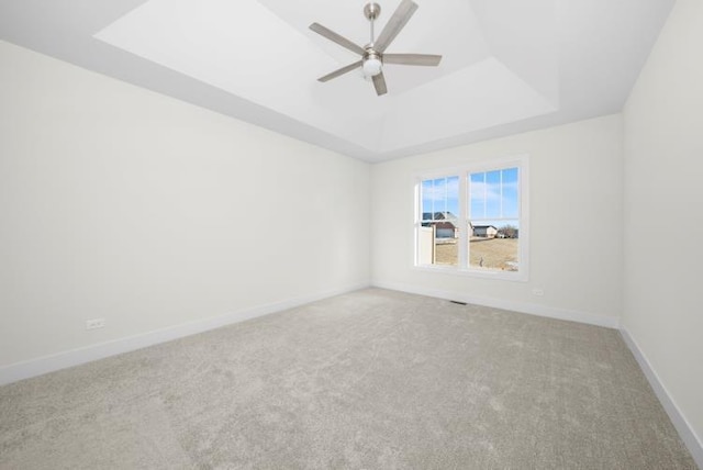 unfurnished room with a raised ceiling, baseboards, carpet, and a ceiling fan