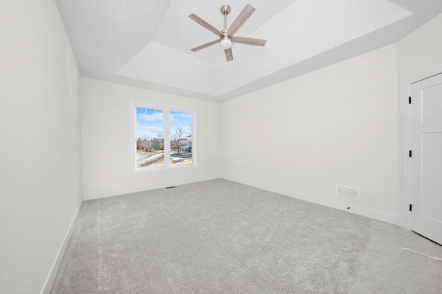 carpeted spare room featuring baseboards, a ceiling fan, a tray ceiling, and visible vents