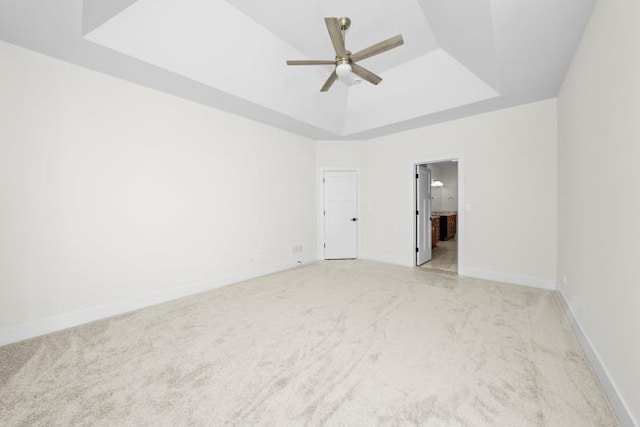 empty room with light colored carpet, a raised ceiling, ceiling fan, and baseboards