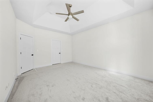 empty room with a ceiling fan, light carpet, and a tray ceiling