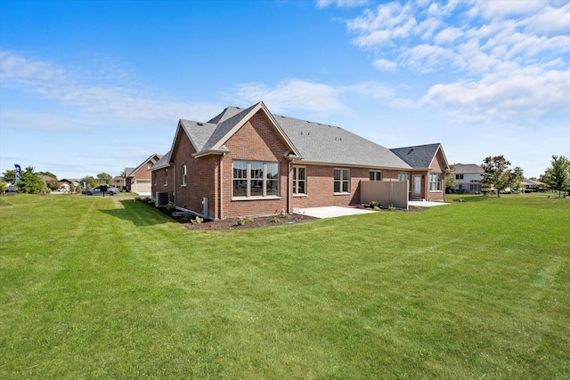 rear view of property featuring roof with shingles, a patio, a yard, and brick siding