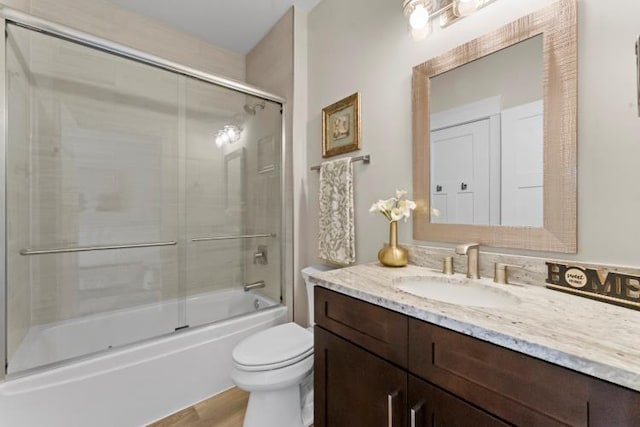 bathroom with toilet, wood finished floors, bath / shower combo with glass door, and vanity