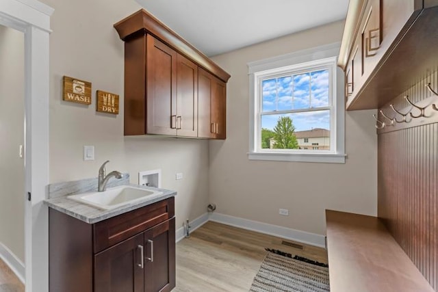 clothes washing area featuring baseboards, hookup for a washing machine, a sink, cabinet space, and light wood finished floors