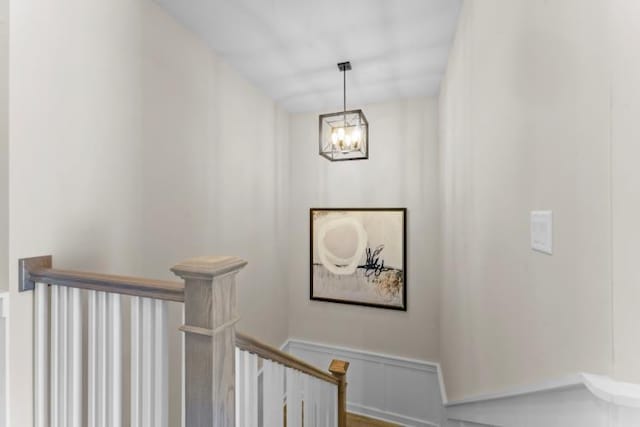 stairs with an inviting chandelier, wainscoting, and a decorative wall