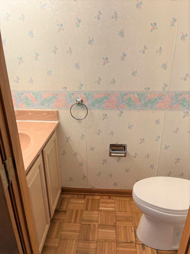 bathroom with vanity, baseboards, toilet, and wallpapered walls