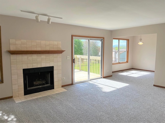 unfurnished living room with track lighting, carpet floors, a tiled fireplace, and baseboards