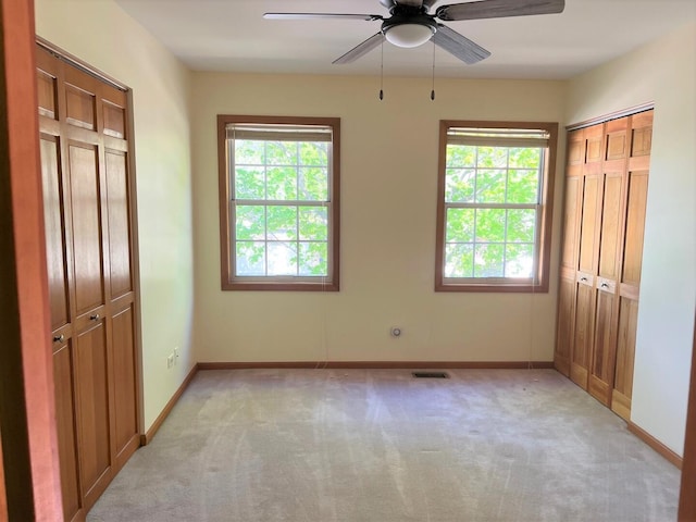 unfurnished bedroom featuring light colored carpet, baseboards, visible vents, and a ceiling fan