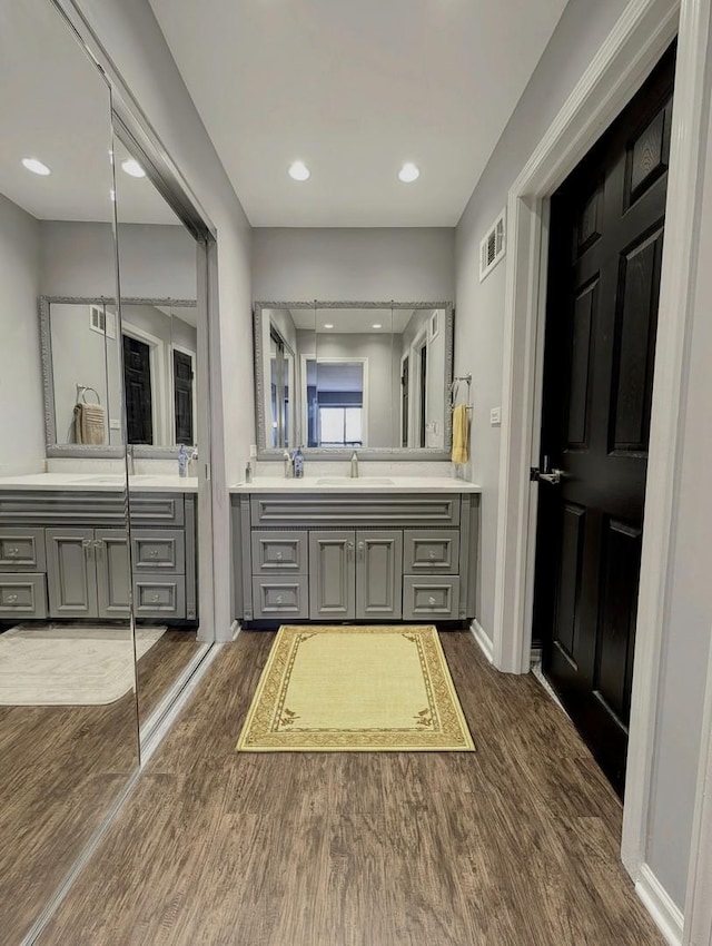 bathroom with visible vents, wood finished floors, two vanities, a sink, and baseboards