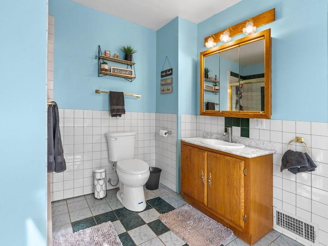 full bath featuring tile walls, a wainscoted wall, tile patterned floors, toilet, and vanity
