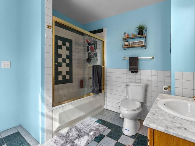 full bathroom featuring tile walls, toilet, enclosed tub / shower combo, vanity, and a wainscoted wall