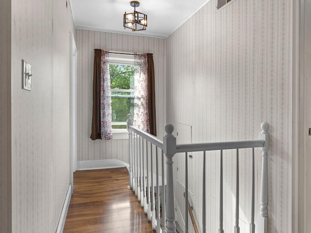 staircase featuring wood finished floors, ornamental molding, wallpapered walls, a chandelier, and baseboards
