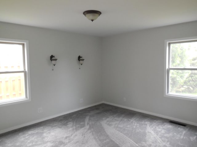 carpeted spare room with baseboards, visible vents, and a wealth of natural light