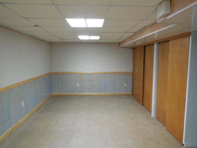finished basement featuring baseboards, a paneled ceiling, and wainscoting