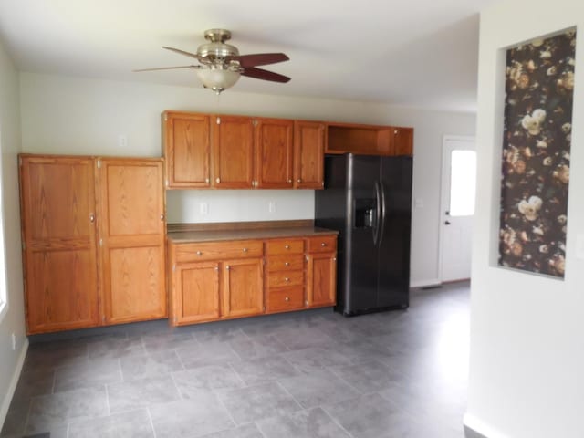 kitchen with ceiling fan, brown cabinetry, baseboards, and black fridge with ice dispenser