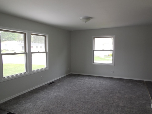 spare room featuring baseboards, visible vents, plenty of natural light, and dark colored carpet