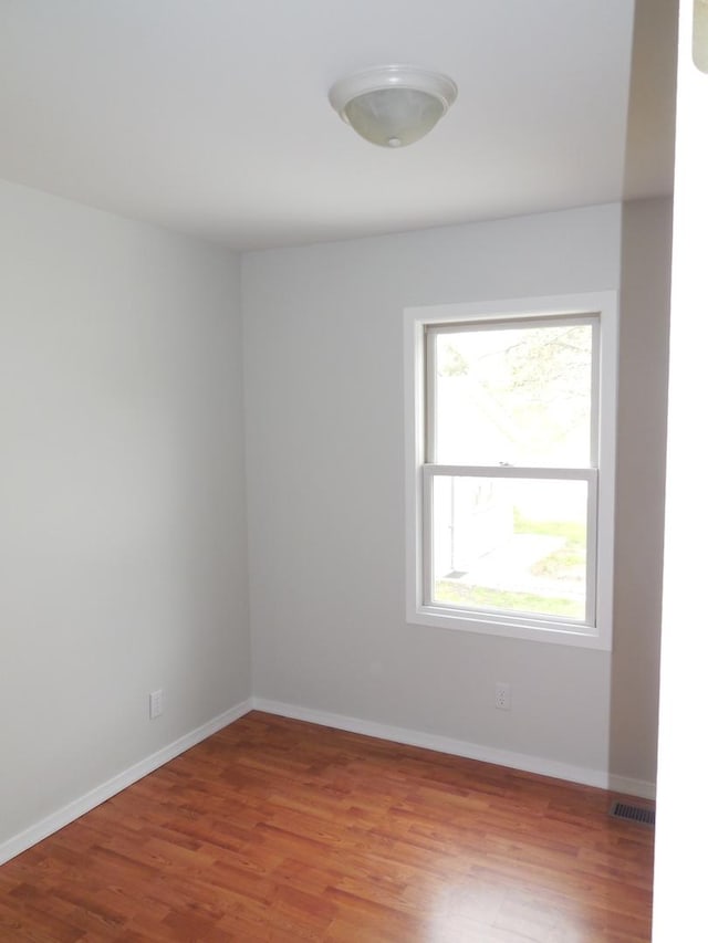 empty room with baseboards, visible vents, and light wood finished floors