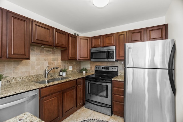 kitchen featuring appliances with stainless steel finishes, a sink, decorative backsplash, and light stone countertops