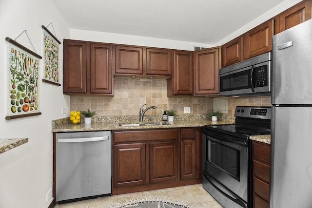 kitchen featuring stainless steel appliances, a sink, tasteful backsplash, and light stone countertops