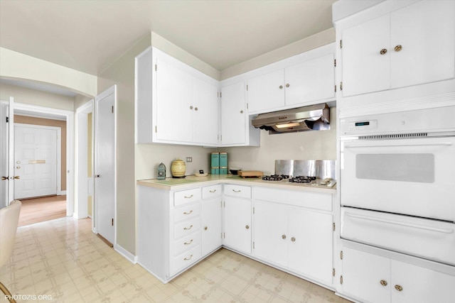 kitchen with light countertops, light floors, a warming drawer, under cabinet range hood, and white appliances
