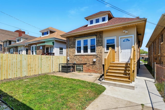 bungalow-style home with central air condition unit, fence, brick siding, entry steps, and a front lawn