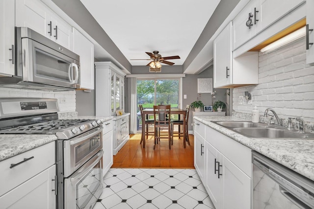 kitchen with a sink, stainless steel appliances, ceiling fan, light countertops, and white cabinets
