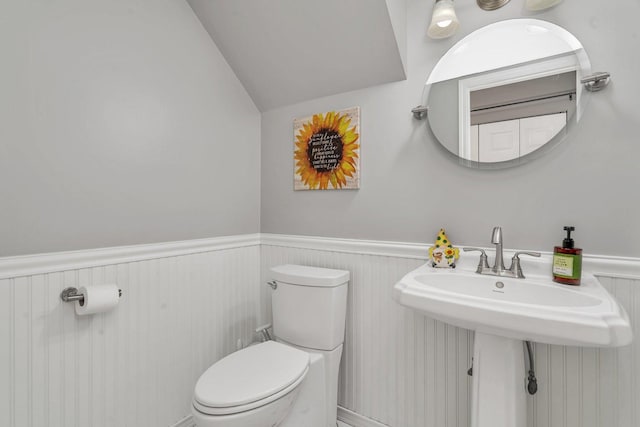 half bath with vaulted ceiling, toilet, and a wainscoted wall
