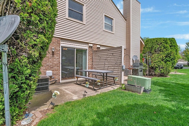 back of house with a lawn, a chimney, brick siding, a patio, and central air condition unit