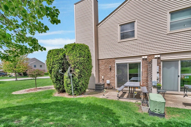 rear view of house with central air condition unit, brick siding, a patio, a chimney, and a lawn