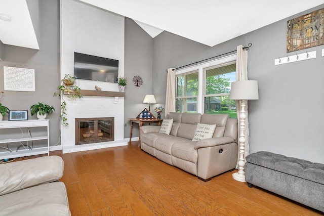 living area with baseboards, a large fireplace, and wood finished floors