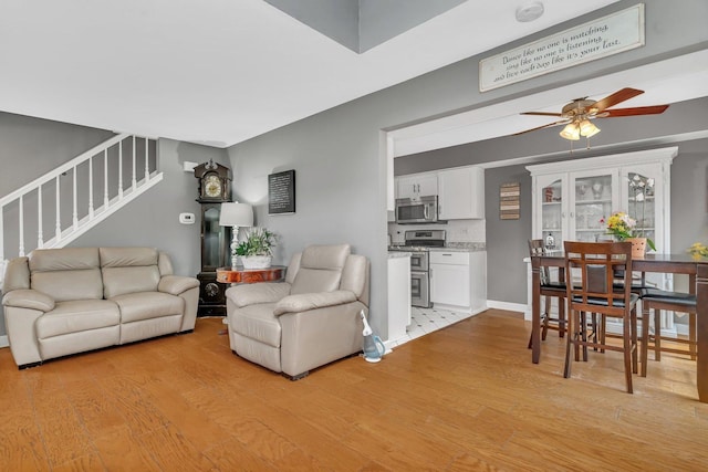 living area featuring light wood-style flooring, stairs, baseboards, and a ceiling fan