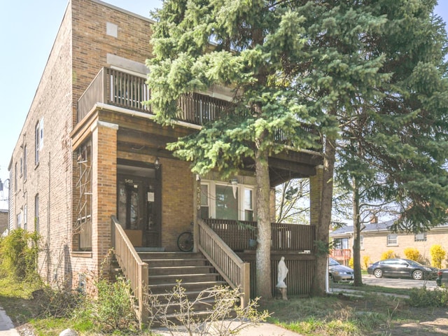 view of front of property featuring a porch, a balcony, brick siding, and stairway