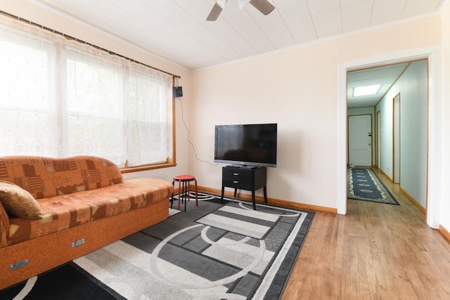 living area featuring crown molding, light wood-style flooring, baseboards, and ceiling fan