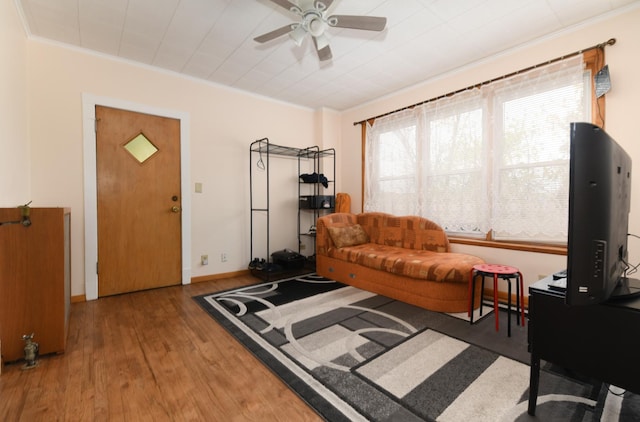 living area with a ceiling fan, ornamental molding, baseboards, and wood finished floors