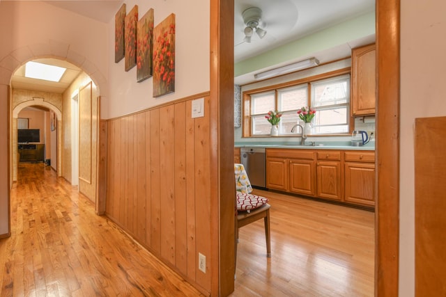 hall with light wood finished floors, wainscoting, a sink, wood walls, and arched walkways